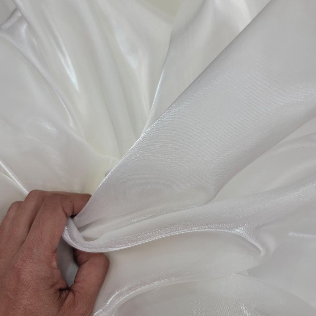 White Organza Fabric: Elegant Style for Dresses and Interiors 27 Close-up of a hand pinching smooth white satin fabric, showing a soft fold and glossy sheen.
