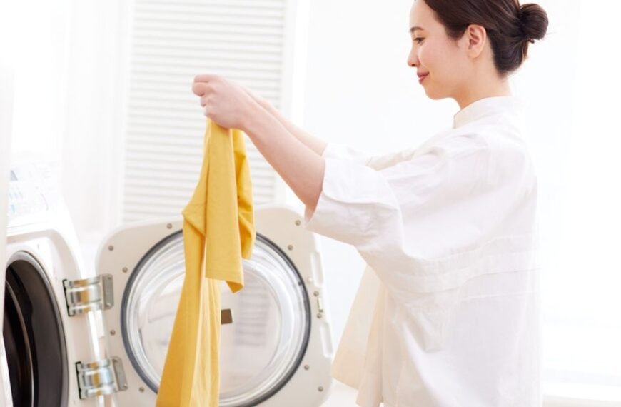 A woman loading a yellow shirt into a front-loading washing machine at home.