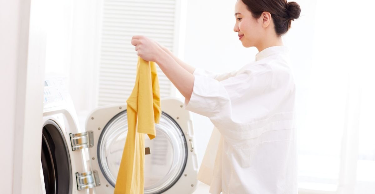 A woman loading a yellow shirt into a front-loading washing machine at home.