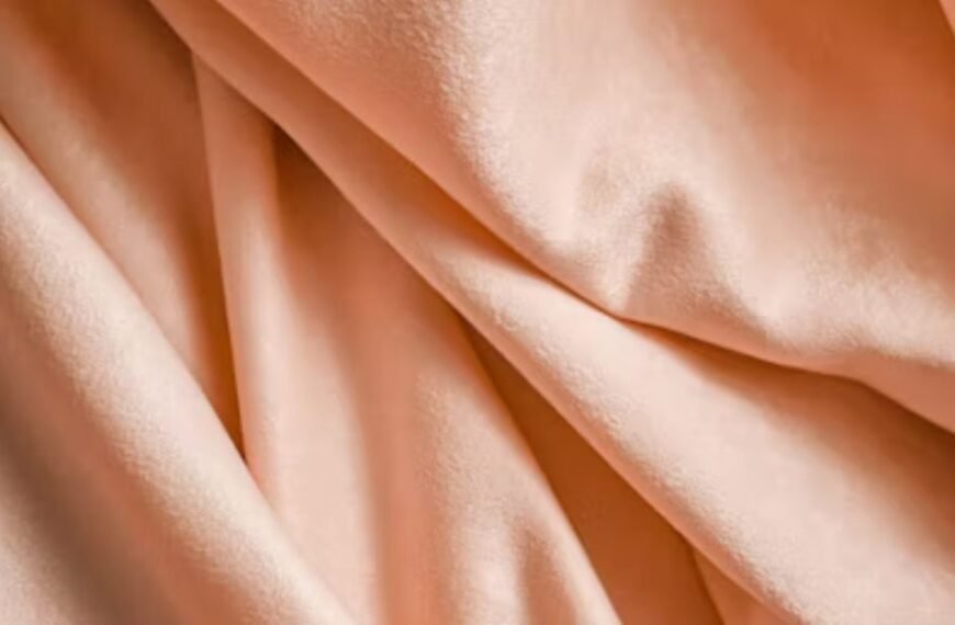 Close-up of soft peach-colored fabric with smooth folds and a silky texture.