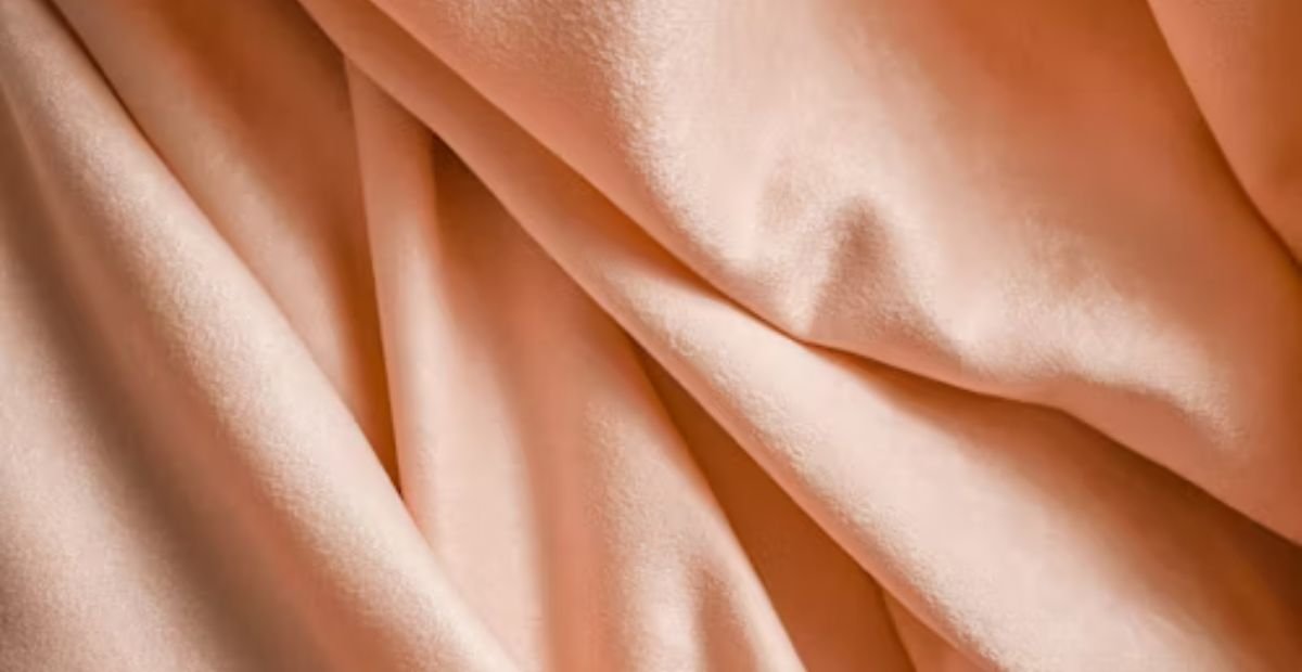 Close-up of soft peach-colored fabric with smooth folds and a silky texture.
