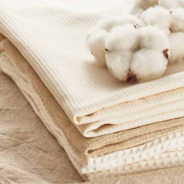 Stack of natural cotton fabrics in neutral tones with a cotton boll placed on top.