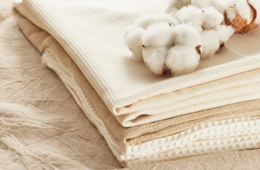 Stack of natural cotton fabrics in neutral tones with a cotton boll placed on top.
