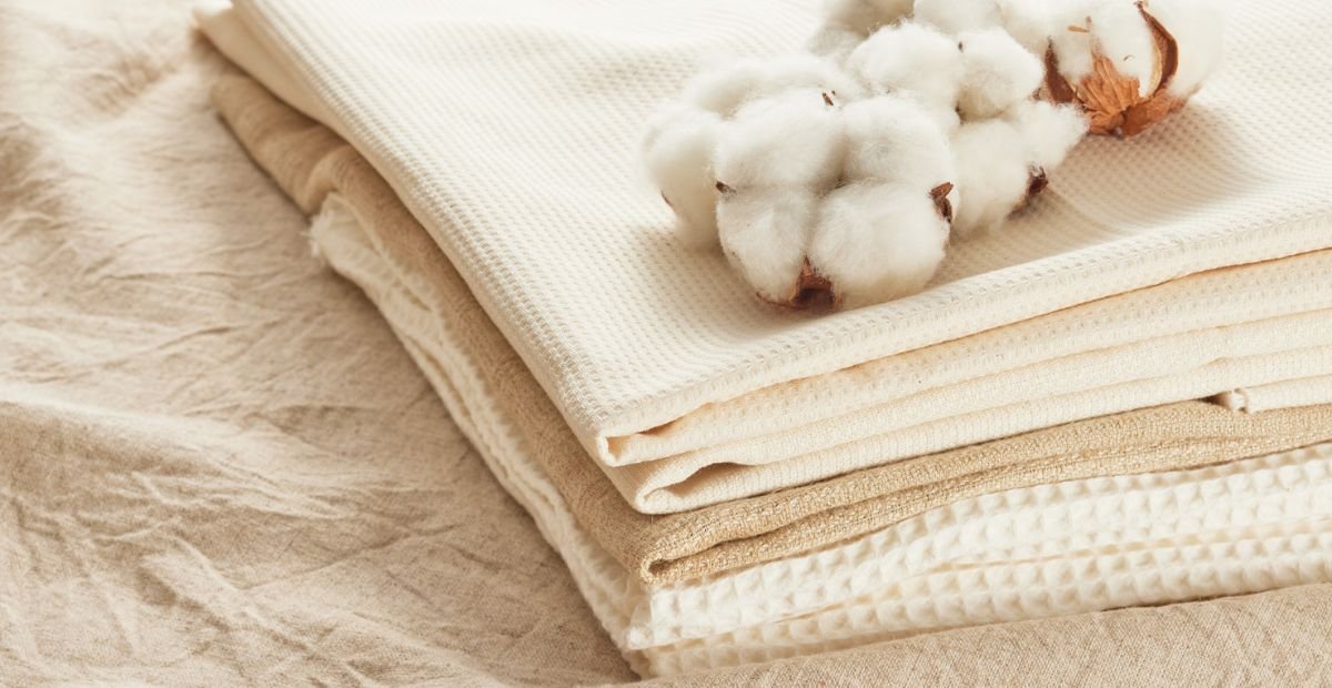 Stack of natural cotton fabrics in neutral tones with a cotton boll placed on top.