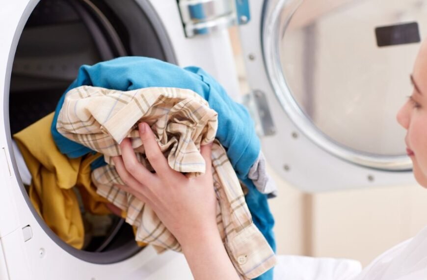 Person loading colorful clothes into a front-loading washing machine.