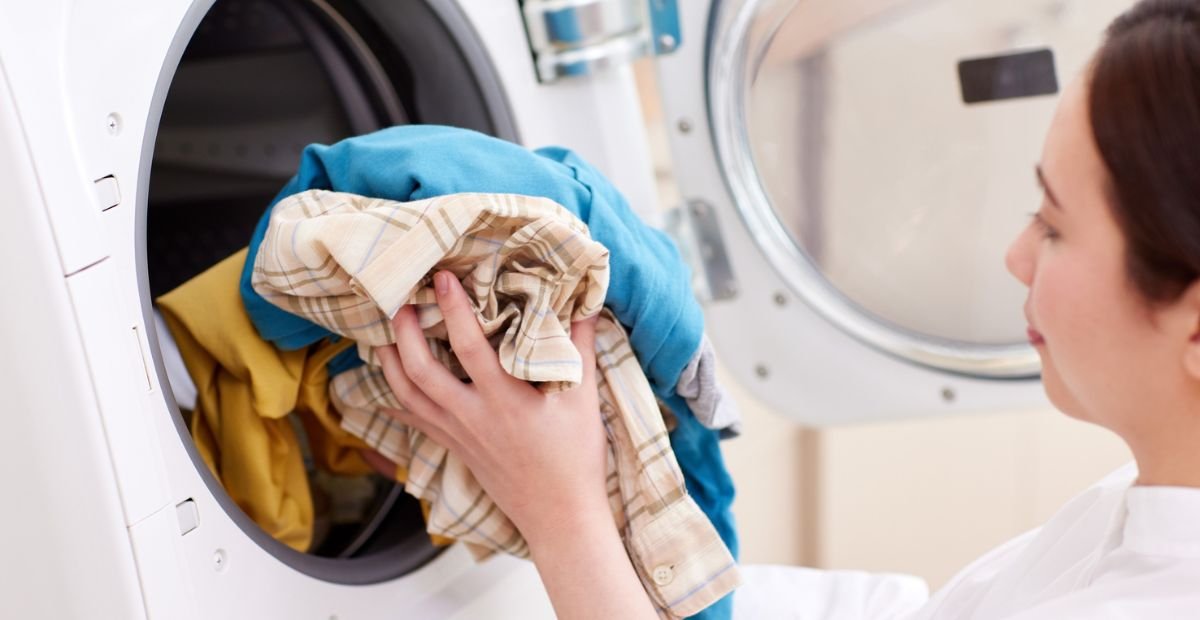 Person loading colorful clothes into a front-loading washing machine.