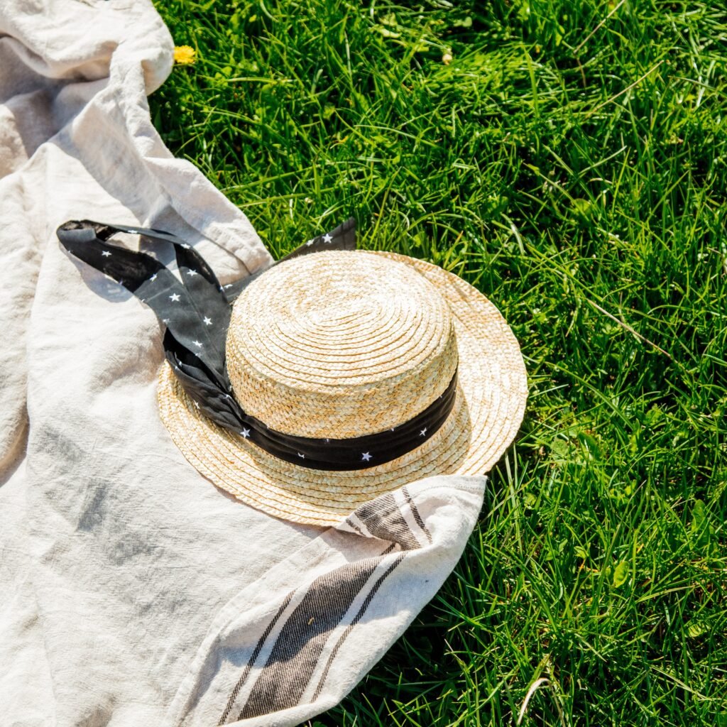 A straw hat and light-colored fabric lie on bright green grass in sunny outdoor conditions, suggesting a summer lawn scene.