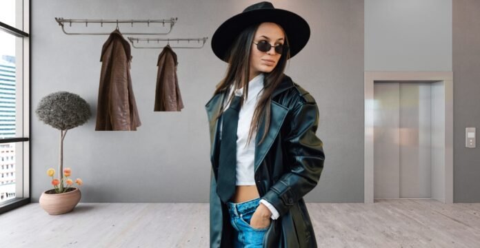 Woman wearing a black leather duster coat, white top, jeans, wide-brim hat, and sunglasses in a modern interior.