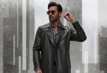 Leather Duster Coat for Men: Timeless Styling TipS A stylish man wearing a black leather duster coat, sunglasses, and a checkered shirt stands against a snowy, abstract geometric background.