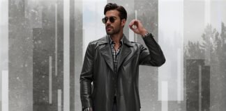 Leather Duster Coat for Men: Timeless Styling TipS A stylish man wearing a black leather duster coat, sunglasses, and a checkered shirt stands against a snowy, abstract geometric background.