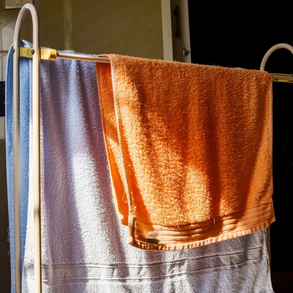 Two towels hanging on a clothes rack: a bright orange towel in front and a light blue towel behind it.
