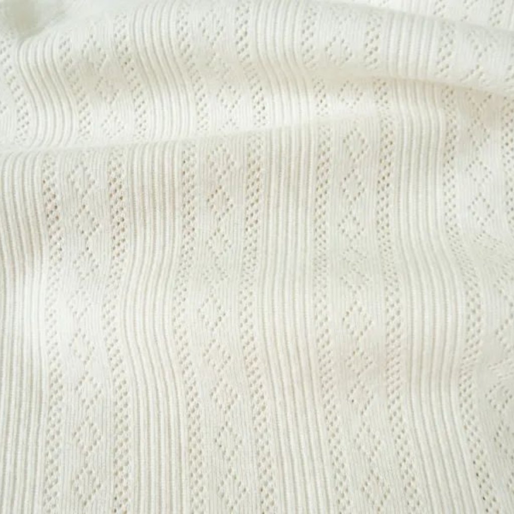 A close-up of white knitted fabric featuring vertical stripes and diamond-shaped openwork patterns.