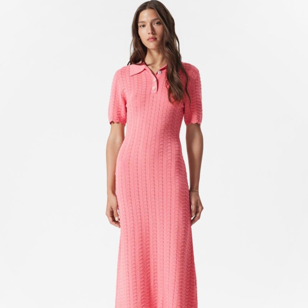 A tall pink knit polo dress on a model, featuring short puff sleeves, a collar, and a subtle chevron/vertical rib pattern that extends to the floor.