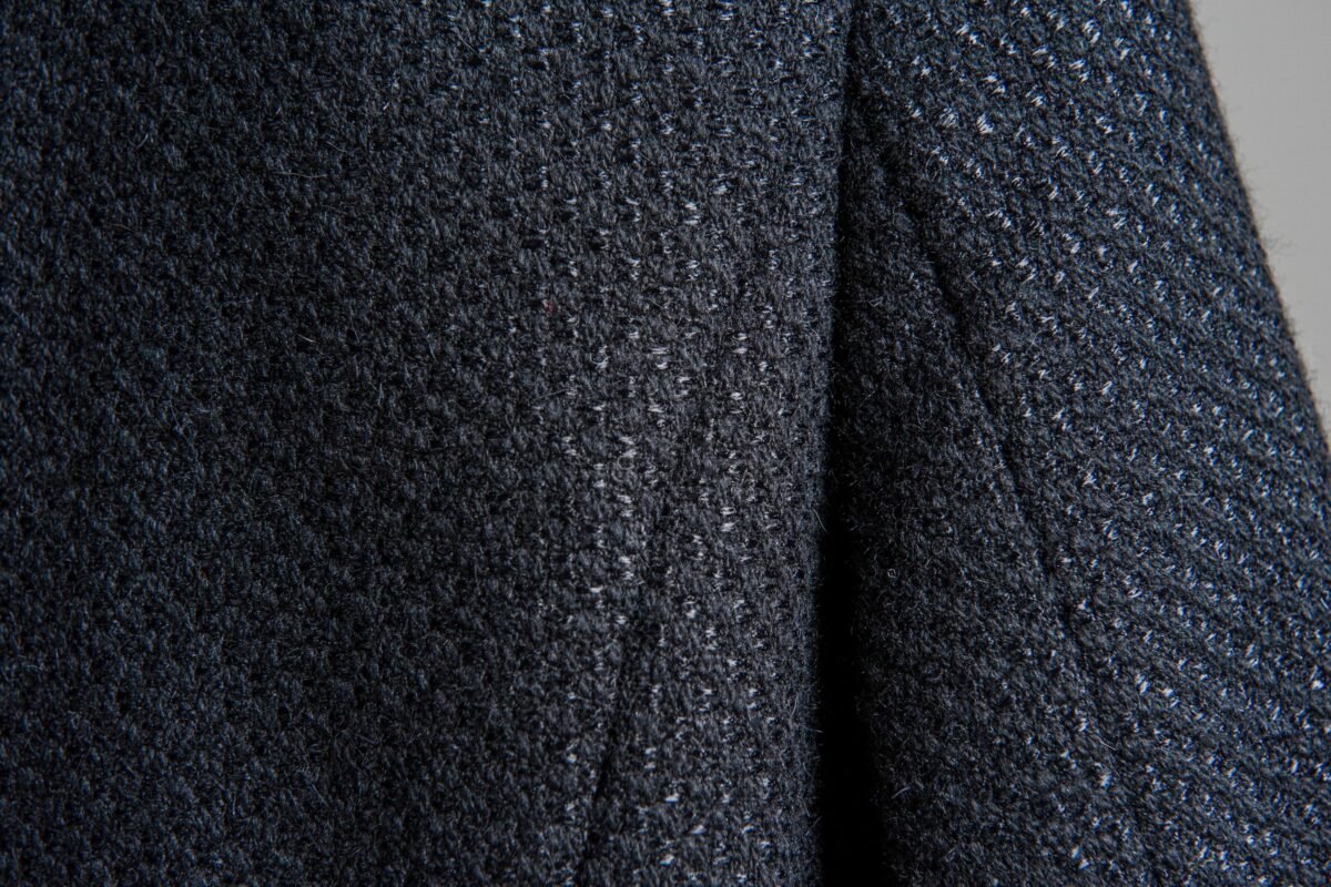 Close-up image of a dark, textured fabric with a speckled, boucle-like surface, showing a soft weave of rayon and nylon fibers.