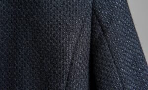 Close-up image of a dark, textured fabric with a speckled, boucle-like surface, showing a soft weave of rayon and nylon fibers.