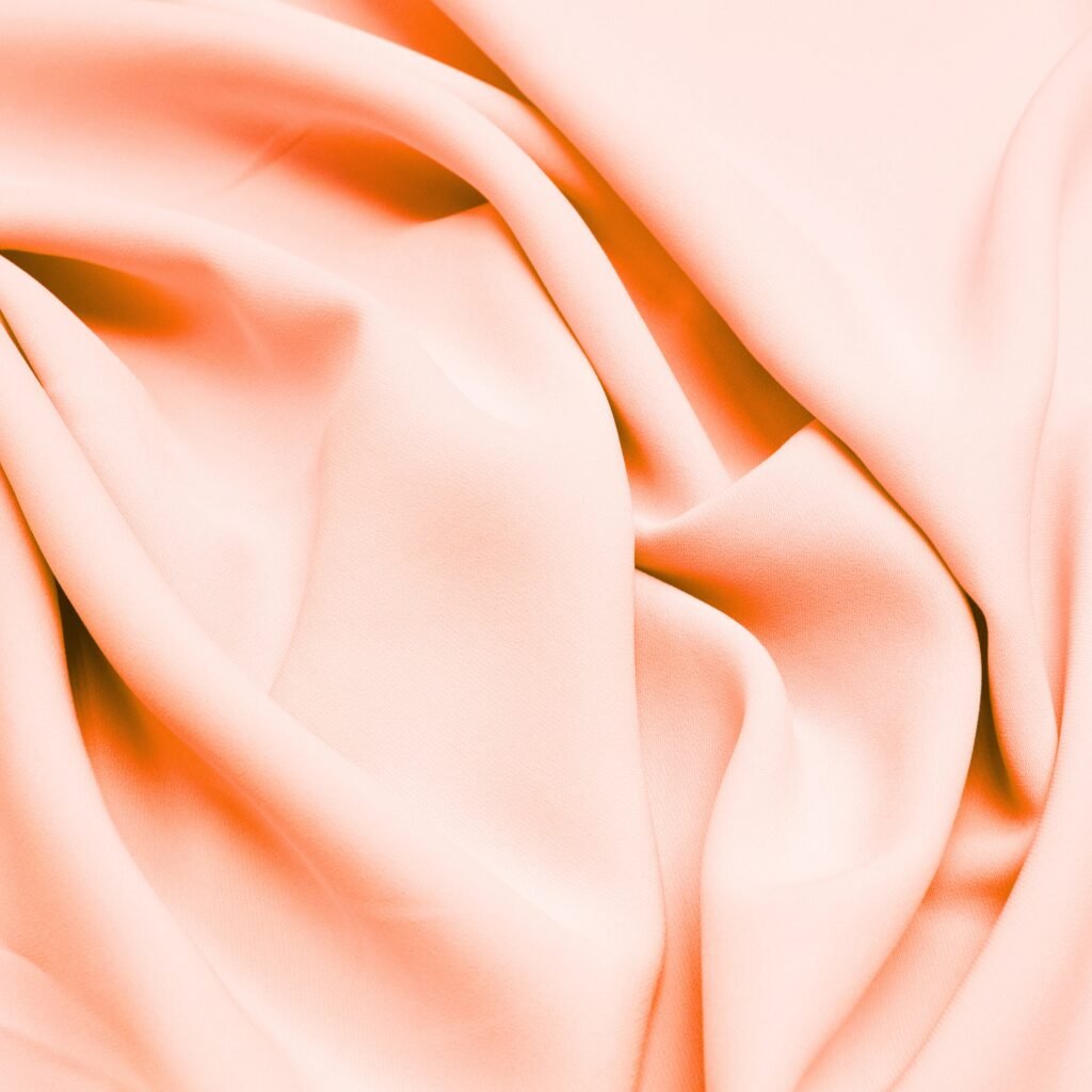 “Close-up of soft peach-pink rayon poplin fabric with gentle folds and smooth, matte surface.”