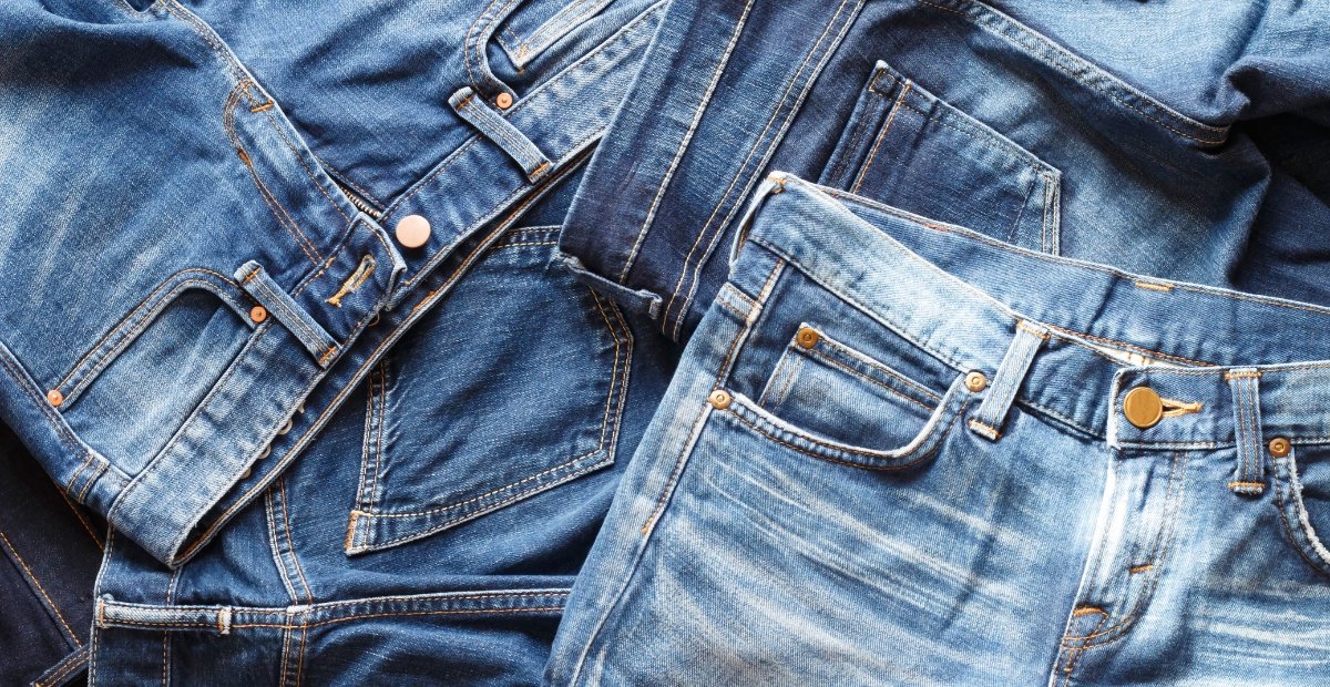 A pile of blue denim jeans with visible stitching, pockets, and copper rivets.