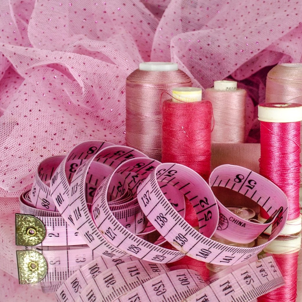 Pink sewing scene with spools of pink thread and a pink measuring tape coiled among fabric.