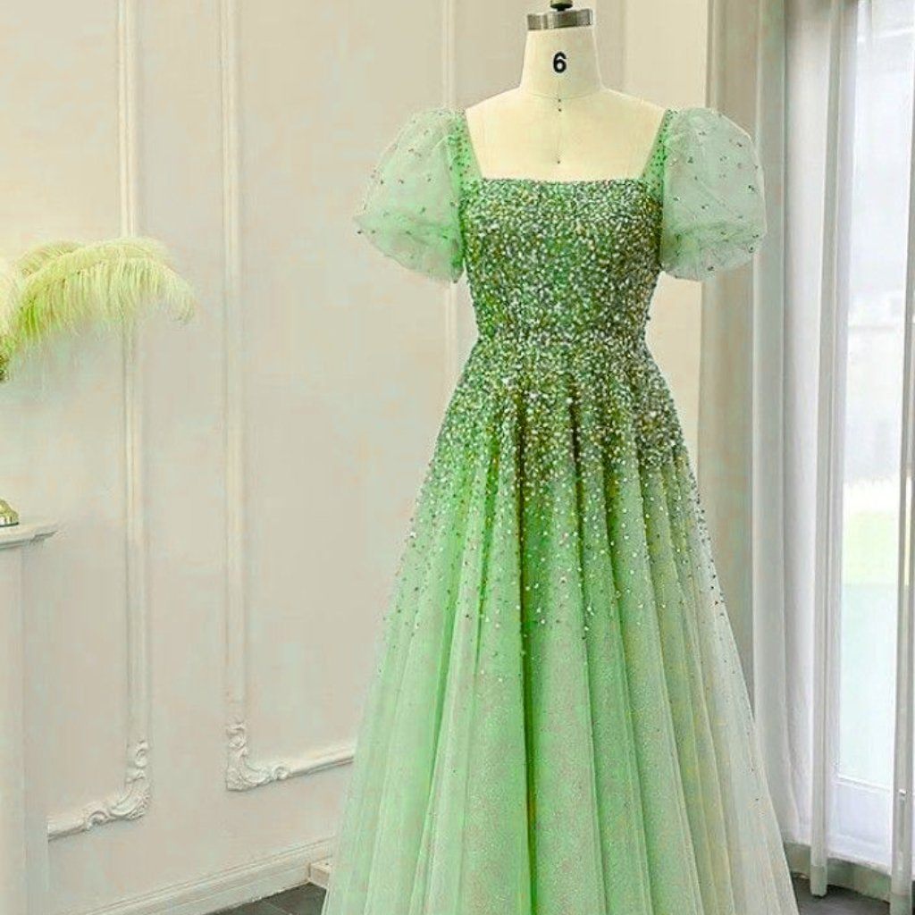 A light-green, floor-length ball gown on a dress form featuring sparkling embroidery and sheer puff sleeves.