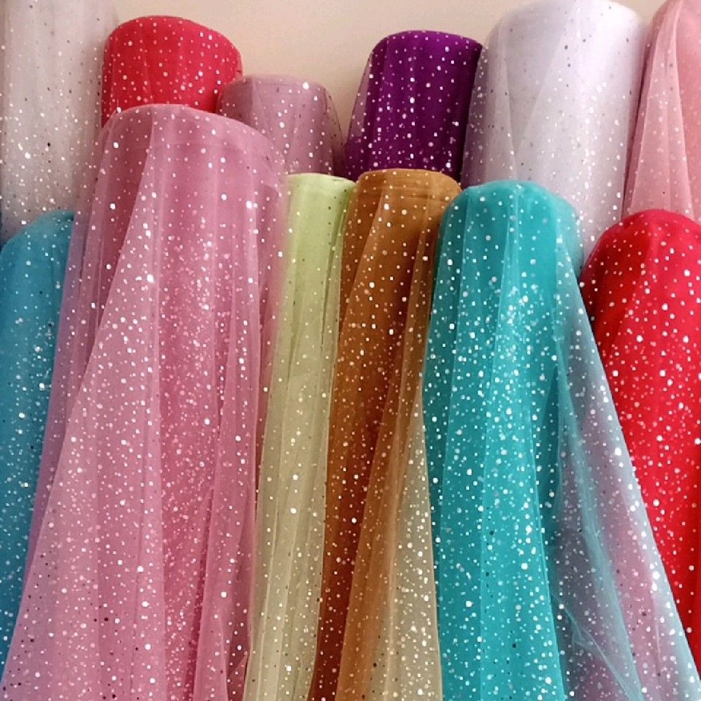 A vibrant display of sheer organza fabrics in a rainbow of colors, each piece sprinkled with tiny white glitter specks, hanging in soft folds.