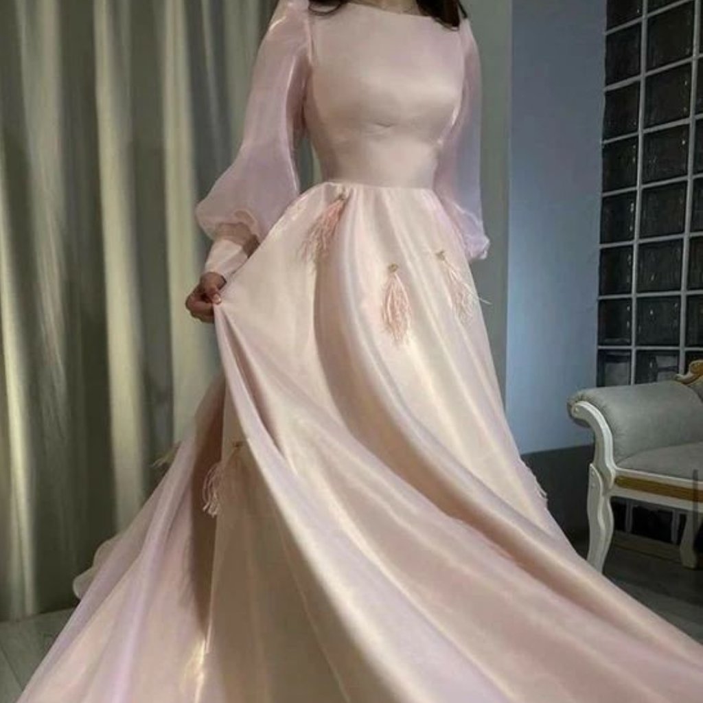 A woman wearing a long, pale pink gown with sheer, billowy sleeves and a full, flowing skirt that trails behind her. The fabric has a smooth, glossy satin texture with subtle sheen.