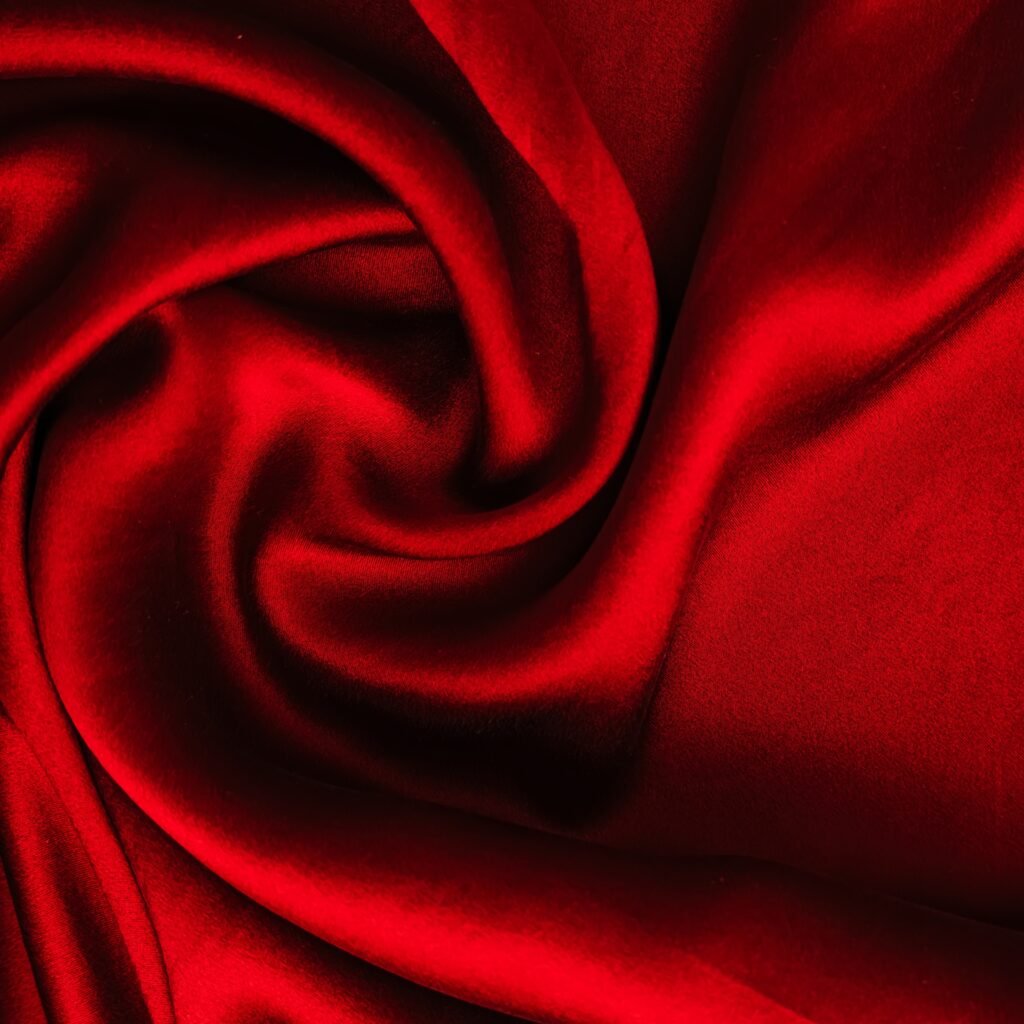 A rich red rayon-silk fabric draped in soft folds, showing a smooth, lustrous surface with subtle sheen and deep shadows.