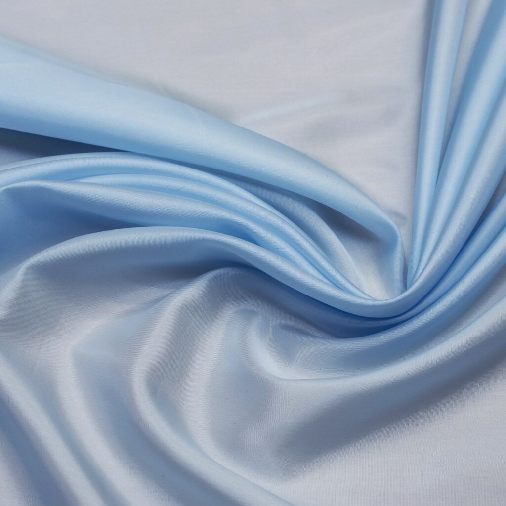 A close-up image of light blue satin fabric draped in soft folds, illustrating rayon’s smooth, glossy appearance.