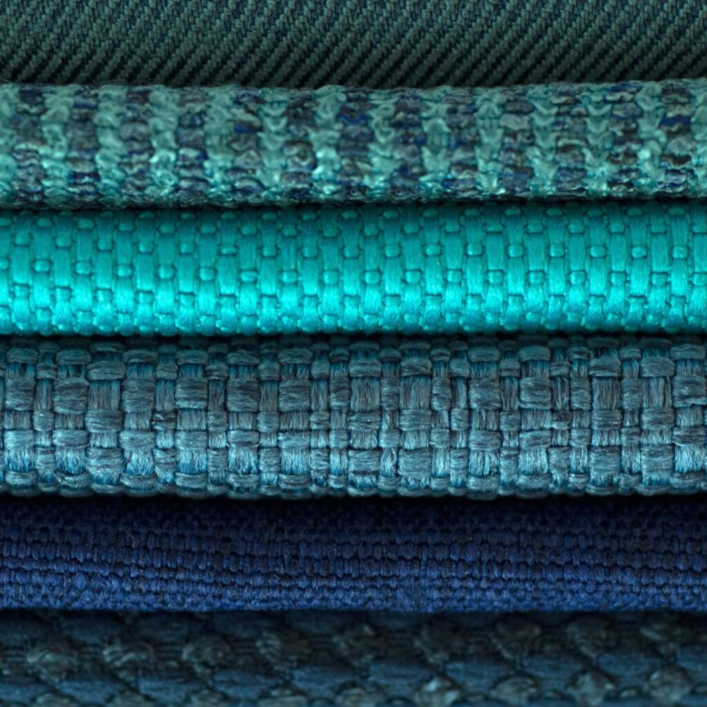 Close-up view of layered fabrics in shades of teal and blue, showing woven textures from fiber to finish.