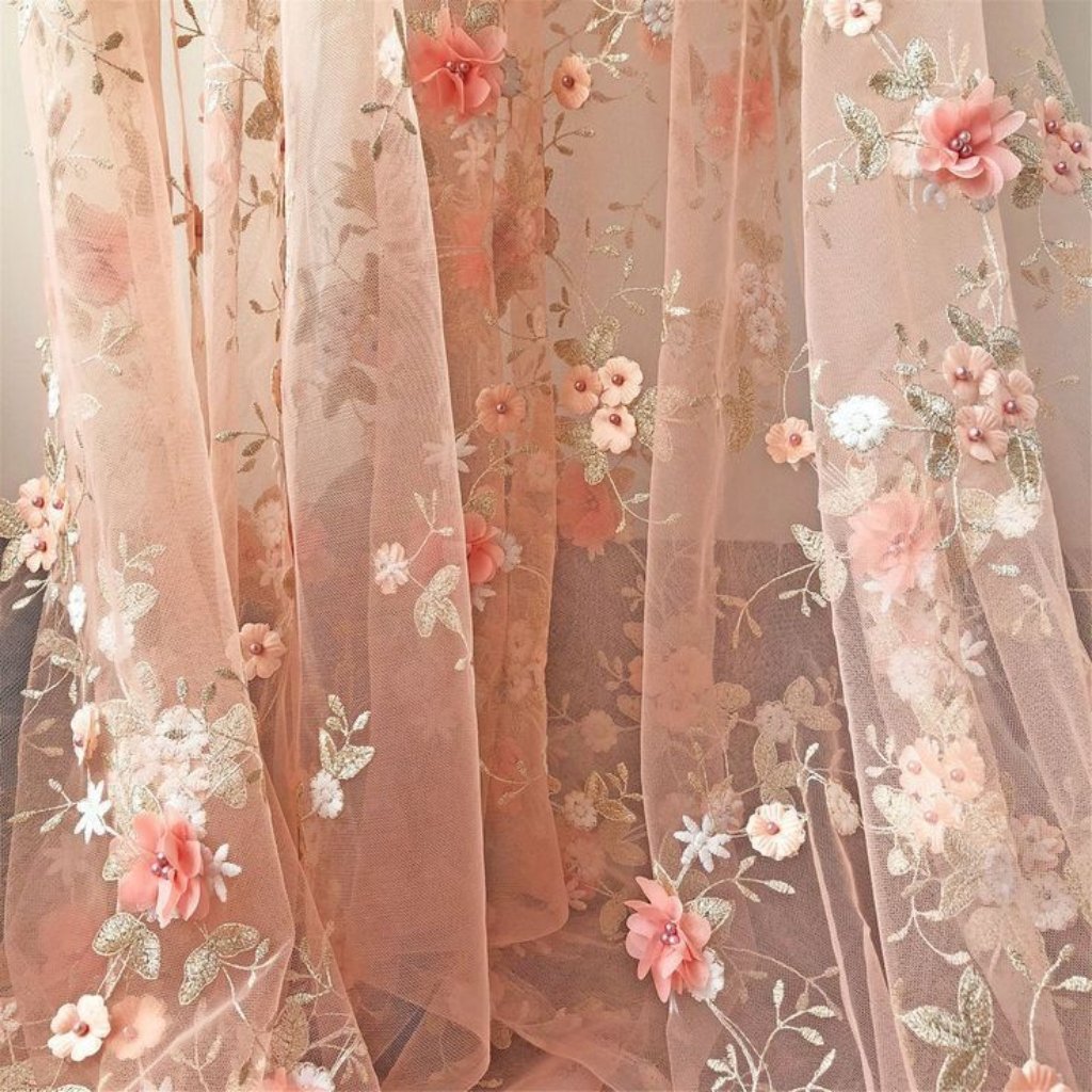 A soft pink sheer curtain or veil with delicate floral embroidery. The fabric features pink and peach blossoms with silver-tinted leaves and tiny bead accents, creating a romantic, dreamy look.

