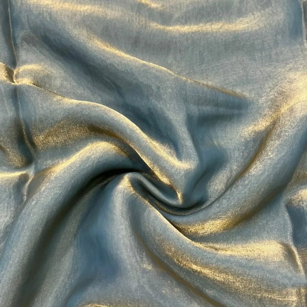 A close-up view of a luxurious, light blue metallic organza fabric. The fabric has a soft, shimmering surface with subtle gold undertones and elegant folds that create gentle curves and highlights.