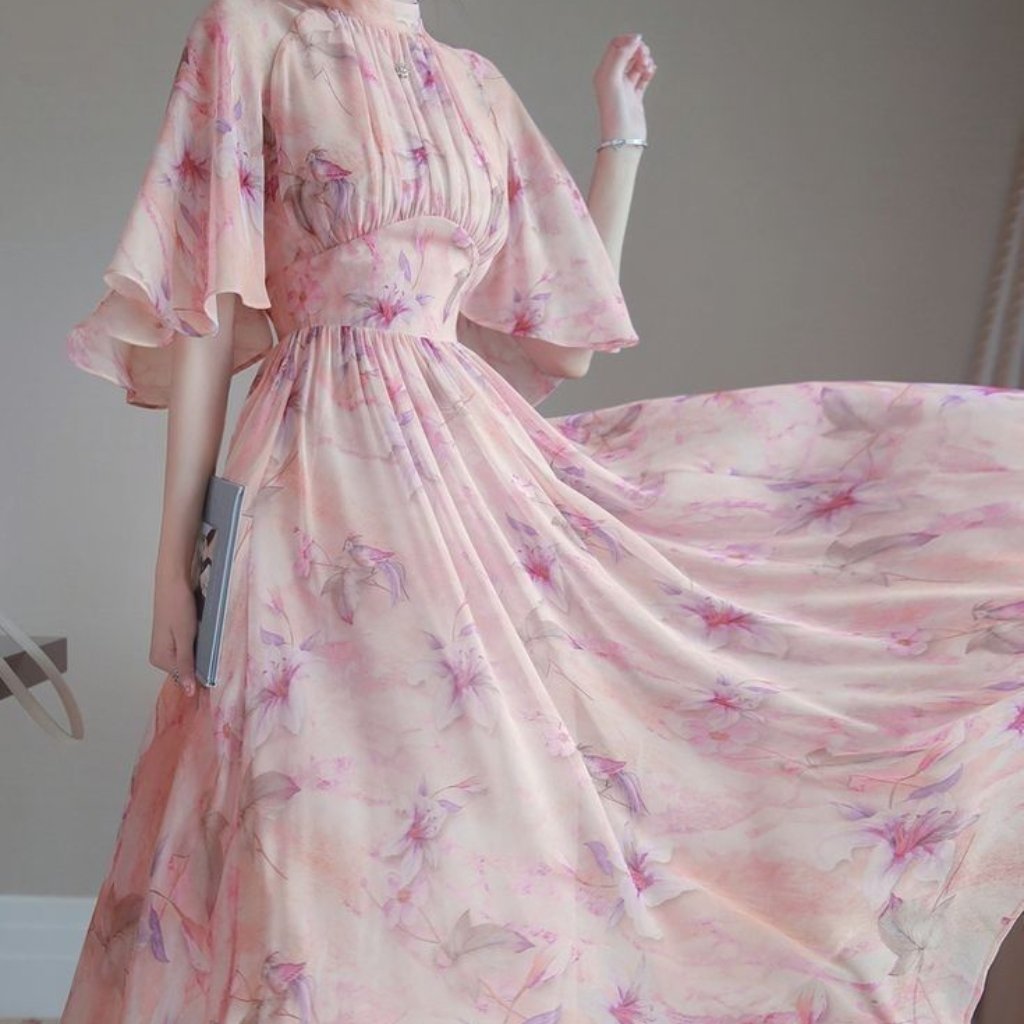 A woman wearing a flowing, pale pink floral dress with soft, billowy sleeves. The dress features a fitted waist and a long, voluminous skirt that moves gracefully as she twirls, creating a dreamy, ethereal look.