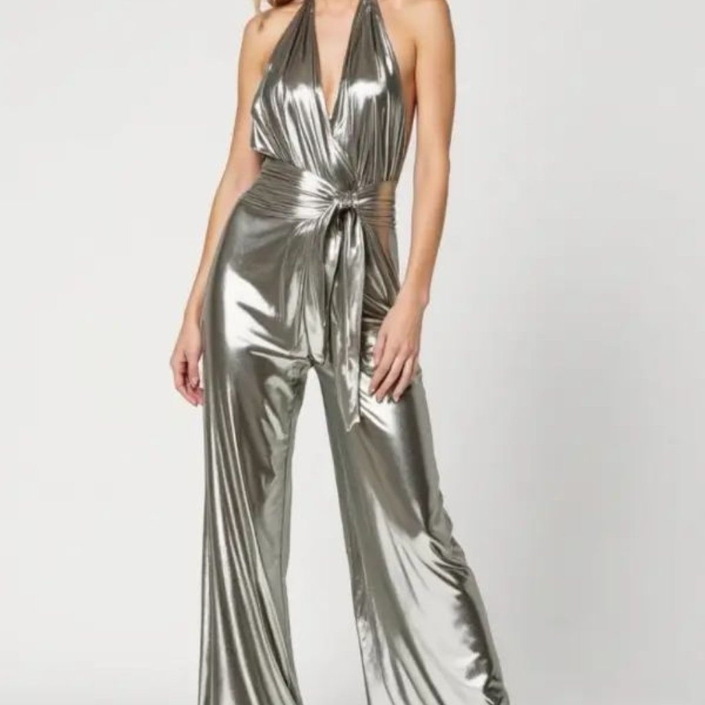 A stylish silver metallic jumpsuit with a deep halter neckline, wide legs, and a wrap-tie belt at the waist. The shiny fabric drapes elegantly, creating a chic, futuristic silhouette.