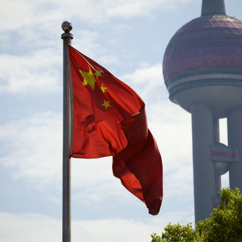 A Chinese flag waving on a flagpole with a modern, spherical building in the background.