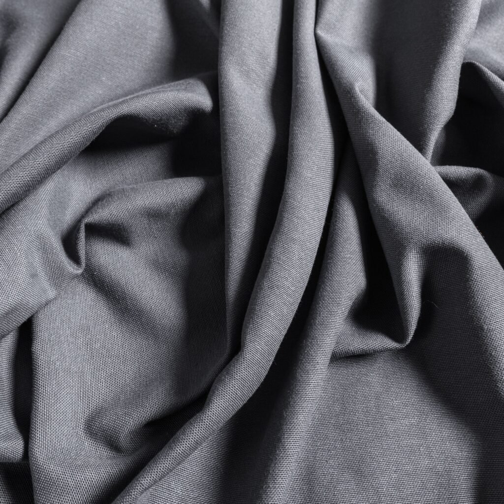 A close-up view of soft, charcoal-gray rayon fabric with folds and gentle drapes.