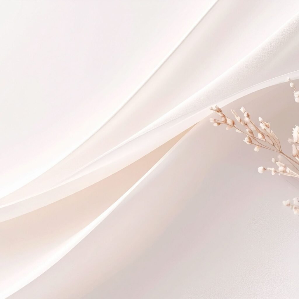 A close-up of a light, airy fabric in soft ivory and champagne tones with delicate draping and a sprig of white dried flowers.