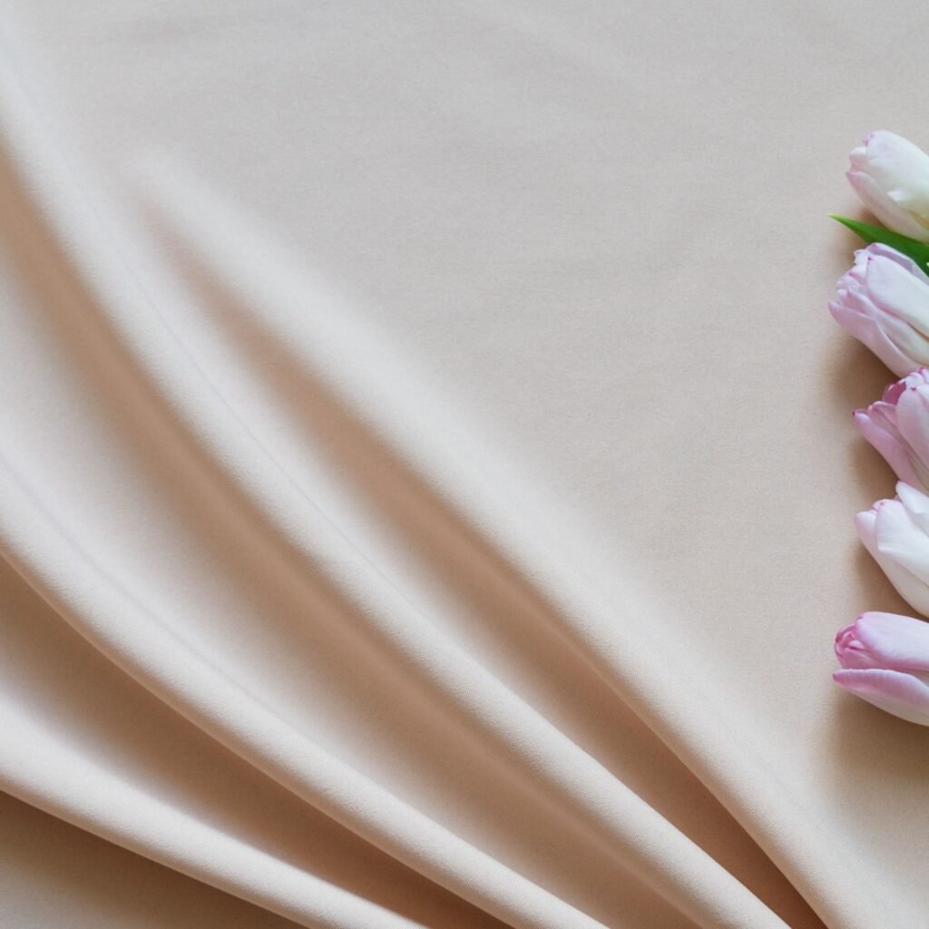 A soft, pale beige fabric draped in gentle folds with a row of pink tulips along the edge.
