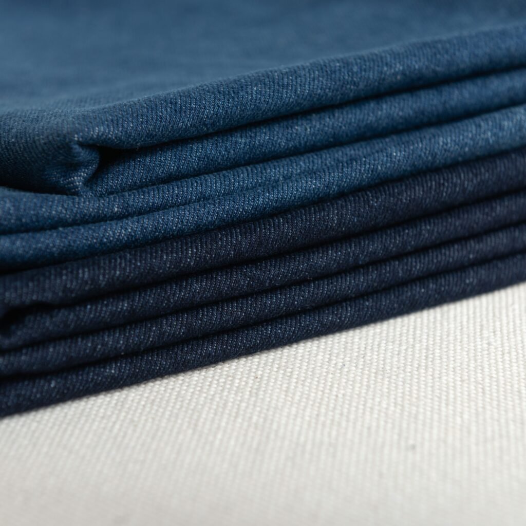 "Close-up view of folded dark blue denim fabric, showing the twill weave and texture."
