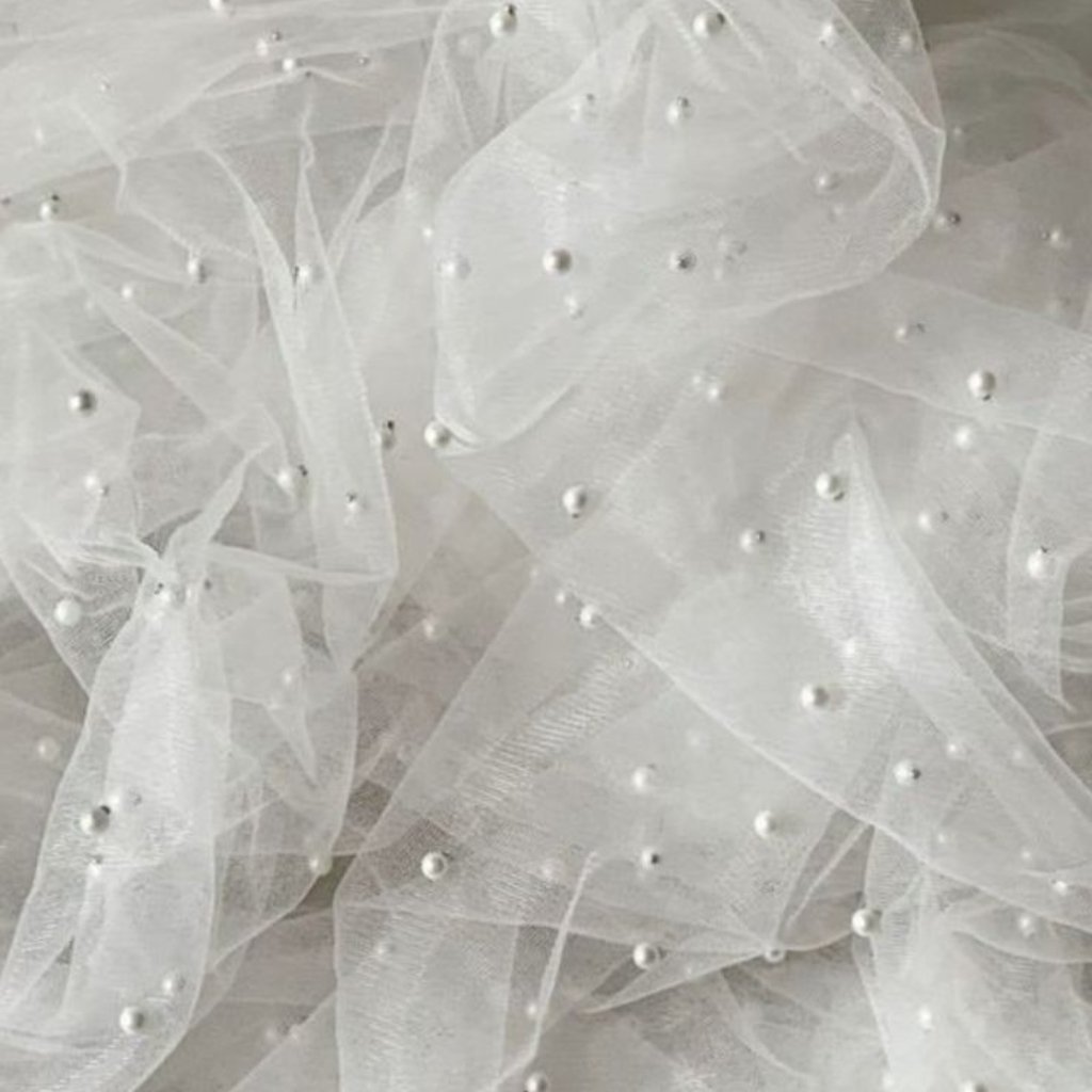 White Organza Fabric: Elegant Style for Dresses and Interiors 17 Close-up image of white sheer tulle fabric with small translucent pearls scattered across the material.