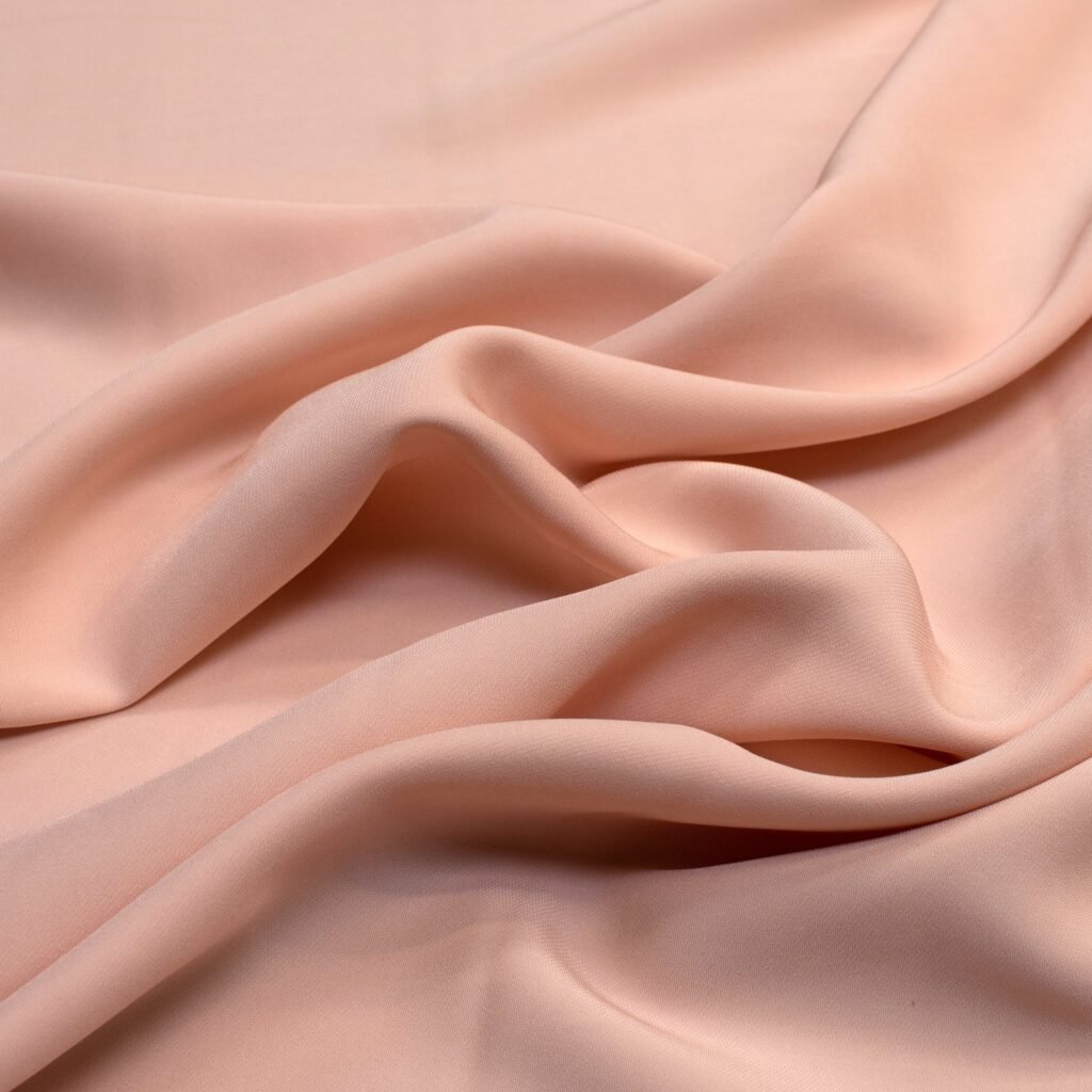 “Soft peach rayon blend fabric draped and curled, smooth and lustrous with subtle folds.”