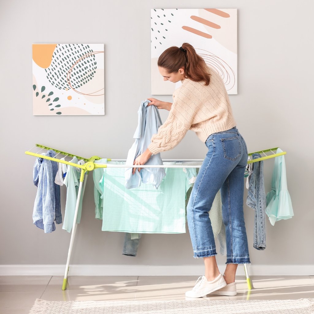 A woman hanging clothes to dry on a portable drying rack in a bright, modern laundry area.