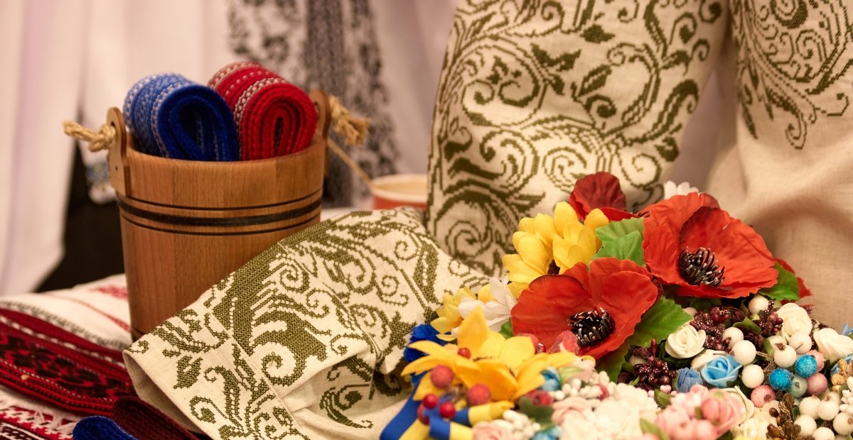 A basket with rolled woven cords beside ornate patterned fabric and a bouquet of colorful artificial flowers.