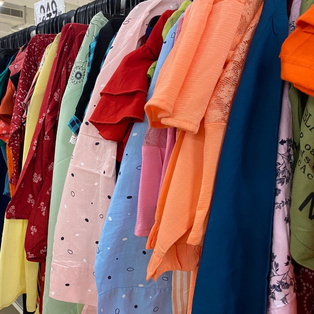 A row of colorful garments hanging on a rack, featuring reds, pinks, blues, and oranges in various patterns and fabrics.