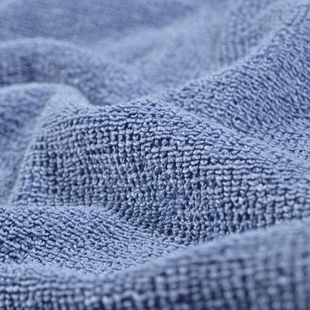 A close-up view of soft, textured blue fabric with thick plush loops and gentle folds.