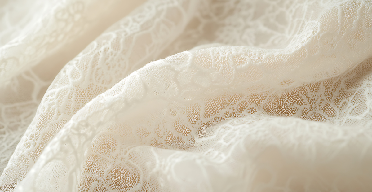 Close-up view of delicate white lace fabric with intricate floral patterns and soft, flowing folds.