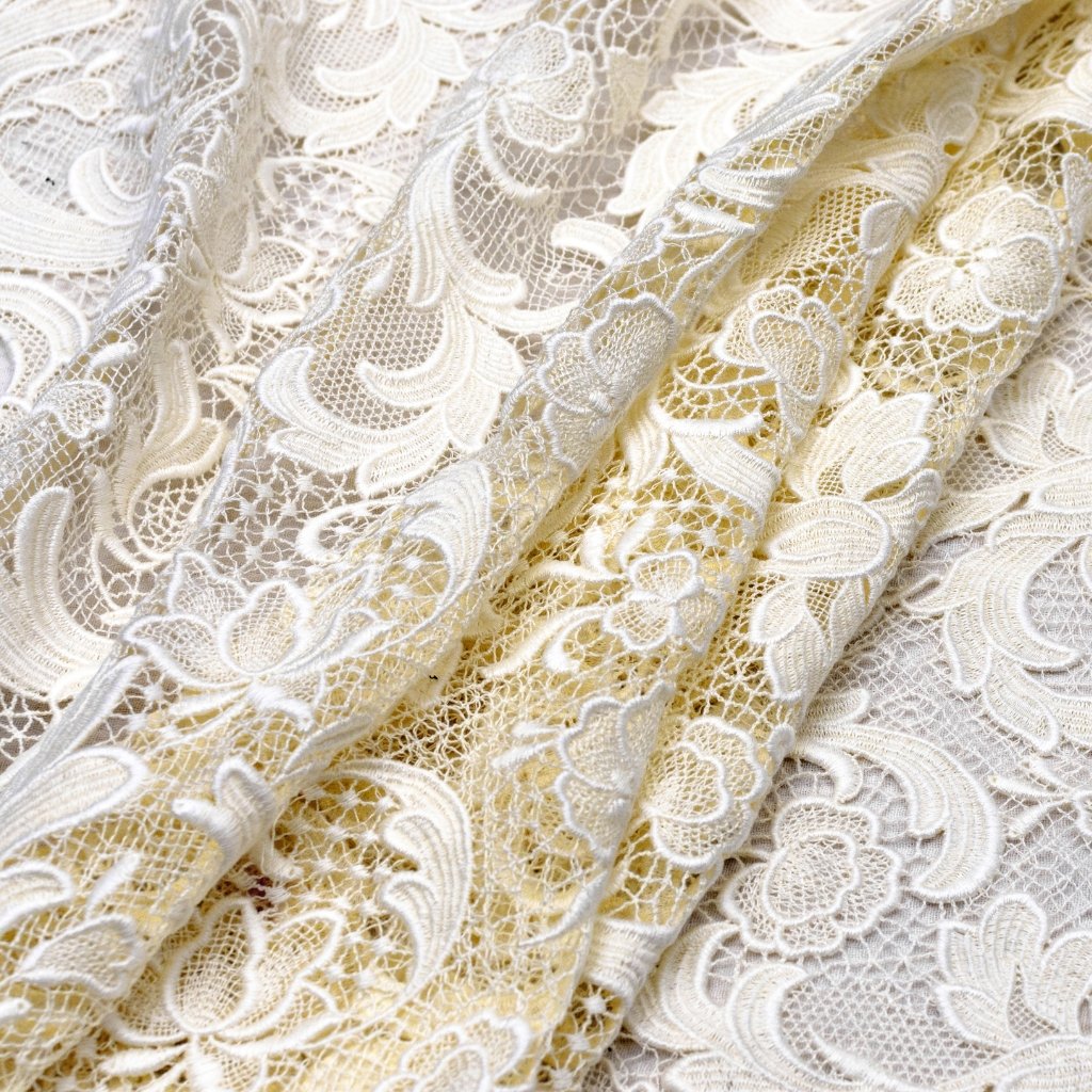 Close-up view of delicate ivory lace fabric with intricate floral patterns and soft folds.

