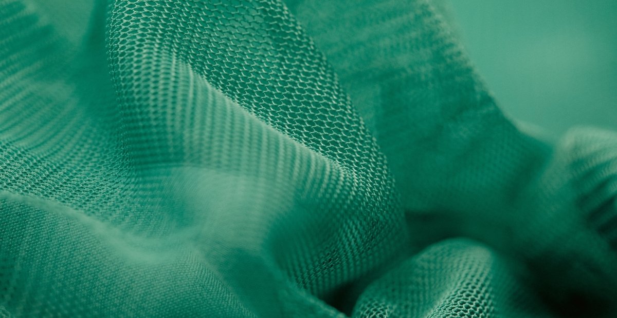 Close-up of green textured fabric or mesh with soft folds and shallow depth of field.