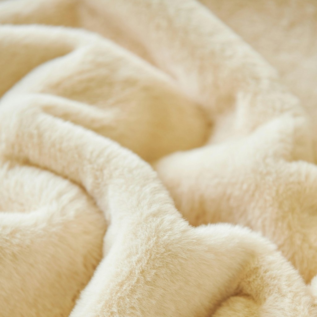Close-up of soft, cream-colored plush blanket with folds and gentle texture.