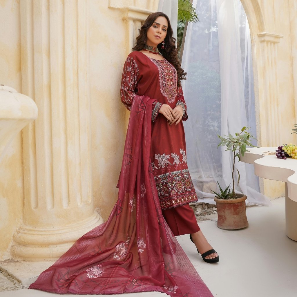 Dimity Cotton Fabric: Soft, Durable, and Timeless Choice 10 A woman in a maroon traditional outfit with intricate embroidery, standing beside a pale yellow column and sheer curtains, holding a matching maroon dupatta.