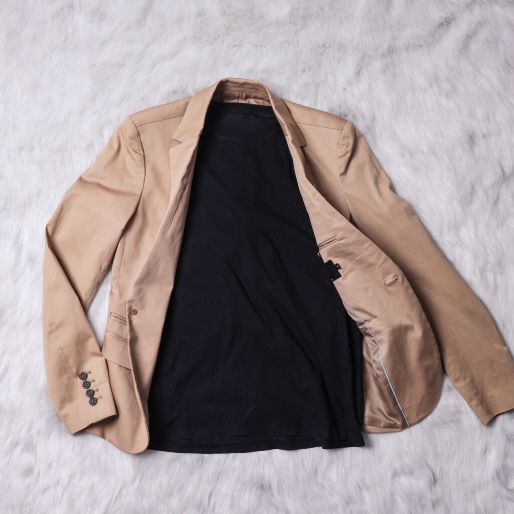 A beige blazer laid open on a light fur surface, showing a black inner lining or shirt underneath.