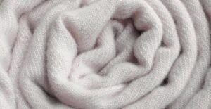 A close-up of a soft, pale pink knit scarf loosely twisted into folds, showing its textured woolen fabric.
